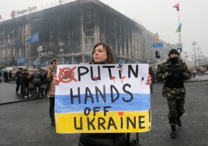 A woman holds a poster against war at Kiev's Independence Square, in Ukraine, Thursday, March 6, 2014. The  Heads of State of the EU will meet Thursday in emergency session in Brussels to discuss the situation in Ukraine. The destroyed trade union offices which was burned in clashes seen in the background  (AP Photo/Efrem Lukatsky)